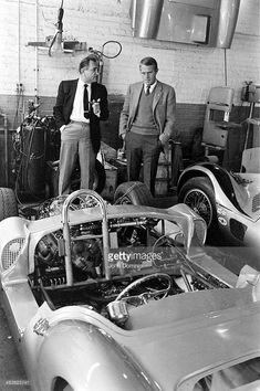 two men looking at an old race car in a garage with another man standing next to it