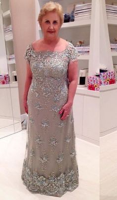 an older woman in a dress standing in front of a store display case and looking at the camera