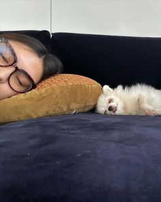 a woman laying on top of a couch next to a small white dog with glasses