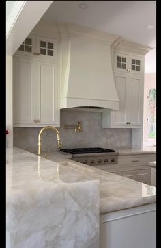 a large kitchen with white cabinets and marble counter tops, gold faucet handles