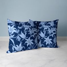 two blue and white pillows sitting on top of a floor next to each other in front of a wall