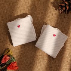 two white napkins with red hearts on them sitting next to some yarn and pine cones