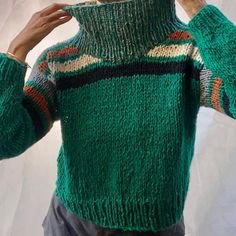 a man is wearing a green sweater with multicolored stripes on it and holding his hands to his face