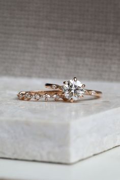 two engagement rings sitting on top of a white marble block with diamonds in the middle