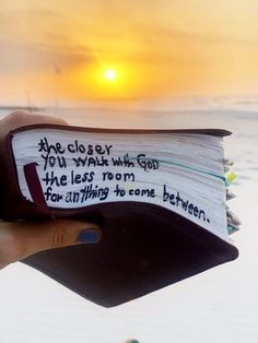 someone is holding up a book with the sun setting in the background and writing on it