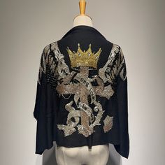 a black jacket with gold sequins and a crown on the back, sitting on a mannequin's head