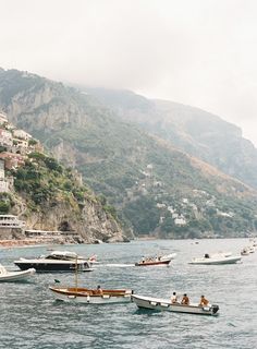 several small boats floating in the water near a city on a hill side with houses