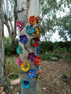 a tree with many colorful flowers on it's trunk in the woods next to some trees