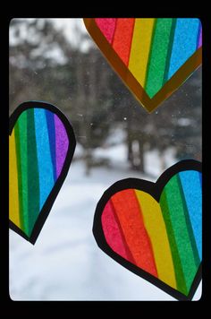 three heart shaped paper cutouts hanging from a window with snow on the ground behind them