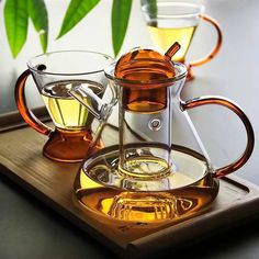 two glass teapots filled with liquid on top of a wooden tray