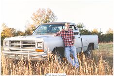 a man standing next to his truck in the middle of a field with tall grass