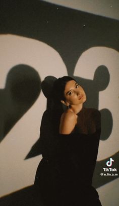 a woman leaning against a wall with her hand on her chin