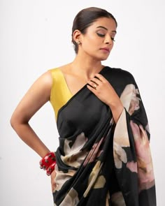 a woman wearing a black and yellow sari with flowers on the side, standing in front of a white background