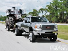 a large truck driving down a road next to a green grass covered field and trees