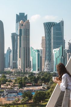 a woman standing on top of a balcony next to tall buildings