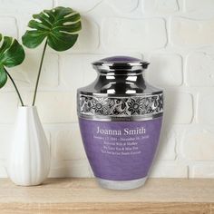 a purple vase sitting on top of a wooden table next to a white vase filled with flowers