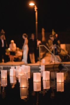 candles are floating in the water with people standing around them and onlookers