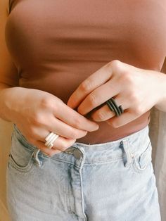 a woman is holding onto her ring while standing in front of a white wall and wearing jeans