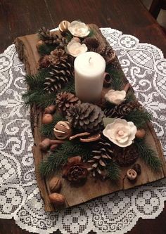 a wooden tray with pine cones, candles and flowers on it sitting on a doily