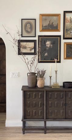 a vase with some flowers on top of a wooden cabinet next to pictures and candles