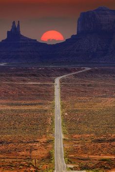 the sun is setting over an empty road in monument national park, utah with mountains in the background