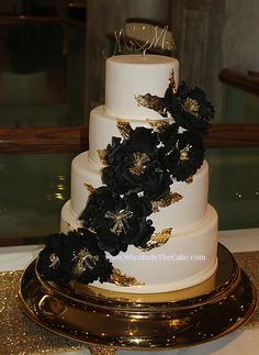 a white and gold wedding cake with black flowers