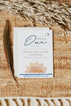 a wedding save the date card sitting on top of a woven mat with a feather