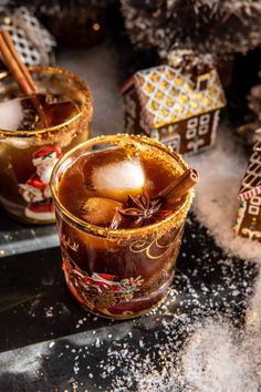 two glasses filled with hot chocolate and cinnamon sitting on top of a table next to christmas decorations