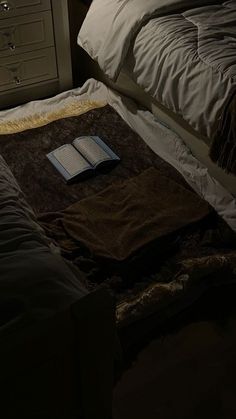 an open book sitting on top of a bed next to a night stand and dresser