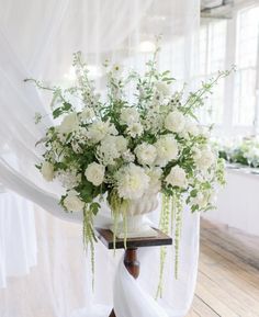 white flowers are in a vase on a table with sheer draping behind it