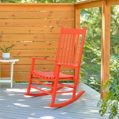 a red rocking chair sitting on top of a wooden deck next to a white table