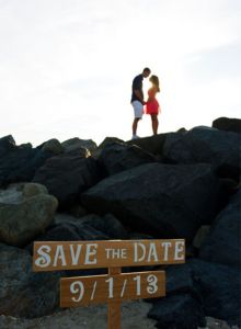 a man and woman standing on top of a rocky beach next to a sign that says save the date