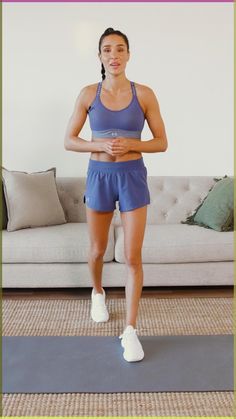 a woman standing on a yoga mat in front of a couch with her hands behind her back