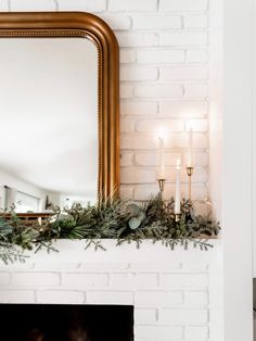 a fireplace with candles and greenery on it