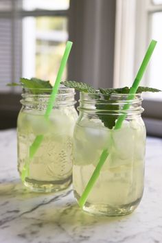 two mason jars filled with lemonade and green straws on top of a table