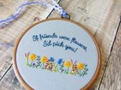 a embroidery hoop hanging on a wooden surface with words written in blue and yellow flowers