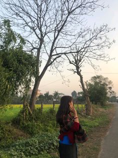 a woman standing on the side of a road talking on a cell phone next to trees