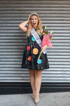 a woman in a black dress holding a pink rose and wearing a tiara with planets on it