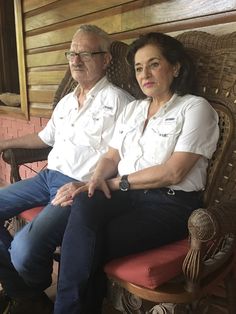 an older man and woman sitting next to each other on a chair in front of a brick wall