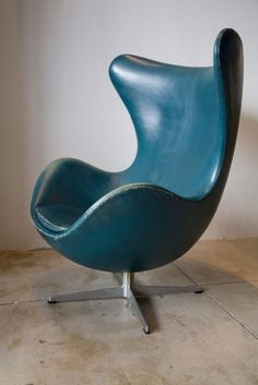 a blue egg chair sitting on top of a metal stand next to a white wall