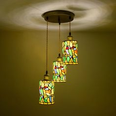 three hanging lights with stained glass shades in a circular light fixture, one is yellow and the other is green