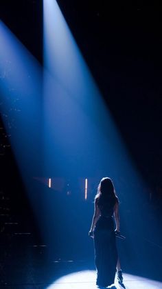 a woman in a long dress walking across a stage with bright blue lights behind her