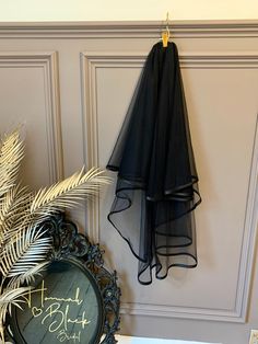 a black dress hanging on the wall next to a mirror and potted palm tree