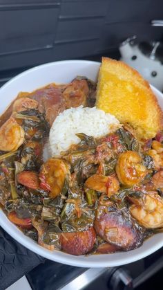 a white bowl filled with rice and shrimp next to a piece of bread on top of a stove