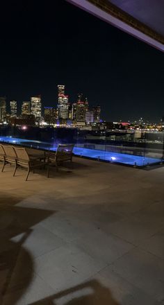 an empty patio with chairs and tables overlooking the city skyline at night, lit up by blue lights