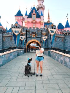 a woman taking a photo with her dog in front of the castle at disneyland world