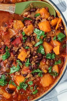 a pot full of chili and beans with a wooden spoon in the top left corner