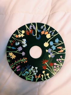 a black plate with flowers painted on it sitting on a white sheet in the bed