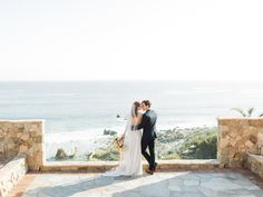 a bride and groom standing on a balcony overlooking the ocean