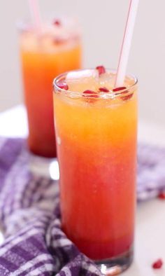 two glasses filled with drinks sitting on top of a purple and white table cloth covered in pomegranates